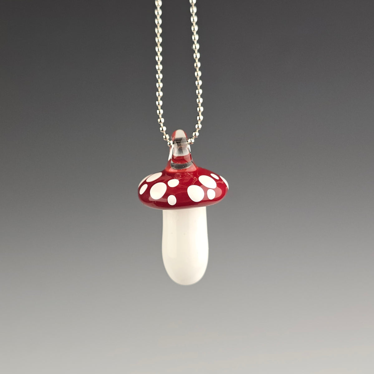 Mushroom-shaped pendant on a chain against a gray background