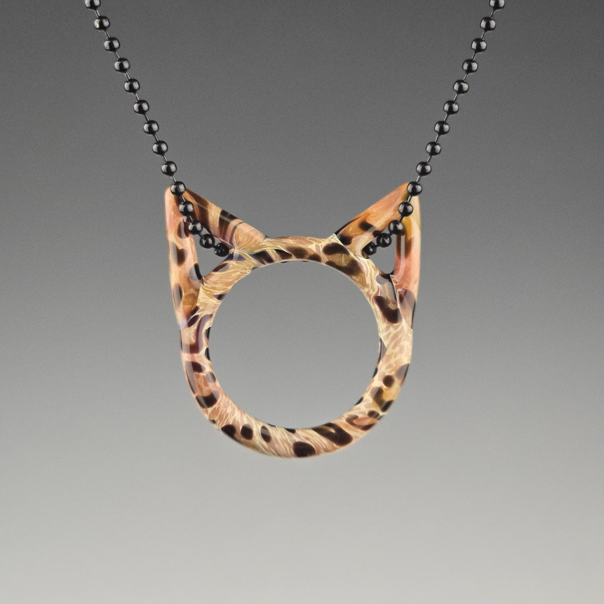 A handcrafted glass pendant in the shape of a kitty face with Bengal cat pattern hanging on a black chain