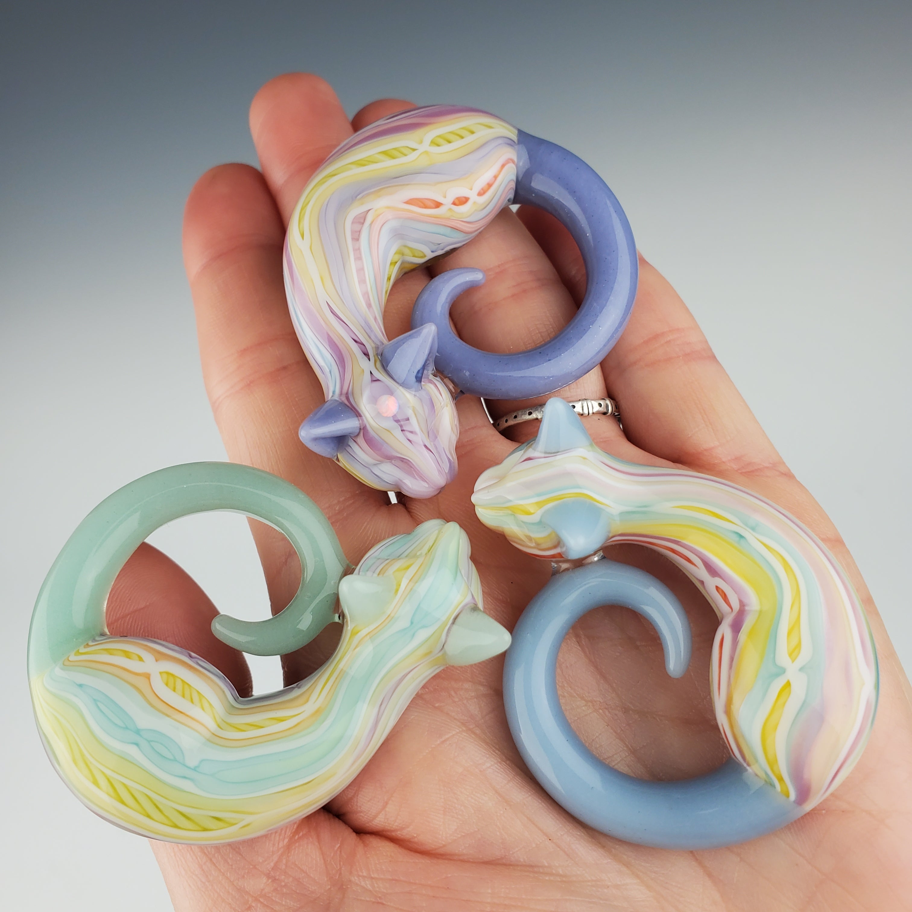 Three Glass Pastel Coogi Sleeping Kitty collaborations by Trip A (Ashley Austin) and Spiller Woods (Annie Woods) being held in the palm of a hand.