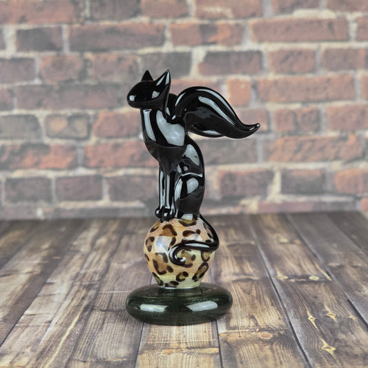 Small glass sculpture of a black cat with wings perched on a marble with leopard print