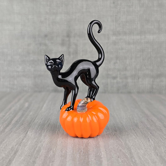 Small glass sculpture of a black halloween cat perched on a glass pumpkin