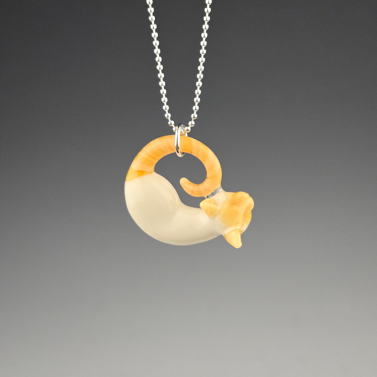 A small glass flame point siamese pendant in the shape of a sleeping kitty 