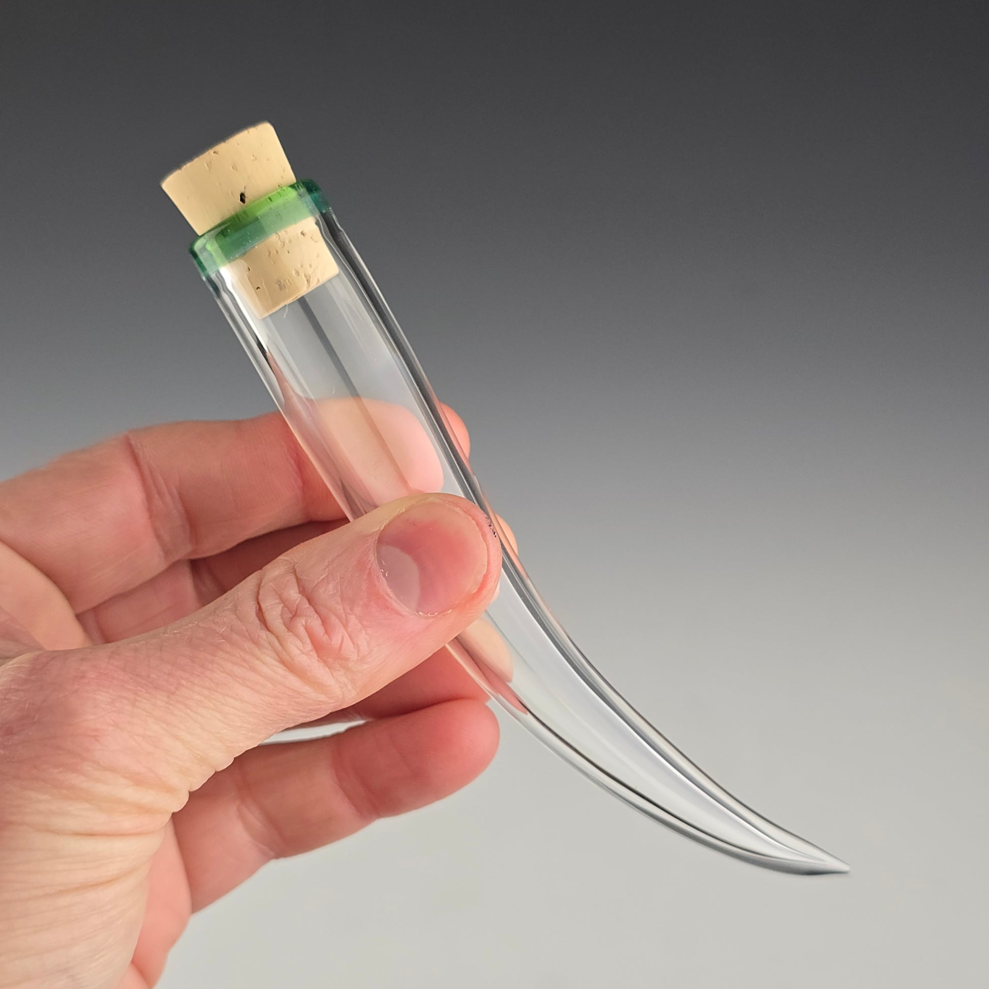 Small hand blown whisker shaped jar made out of clear glass with a meta Terrania green color accent around the corked opening. This is a safe special place to keep the fallen whiskers you find.