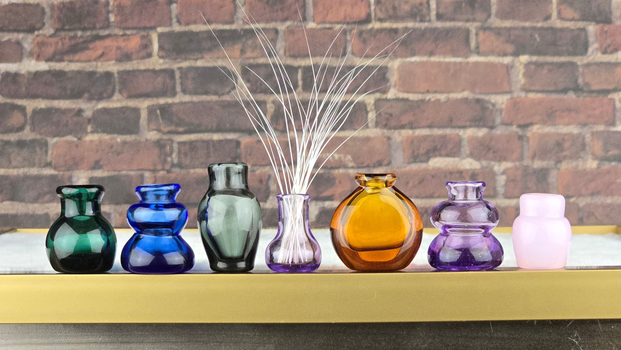 Colorful glass whisker vases on a shelf against a brick wall.