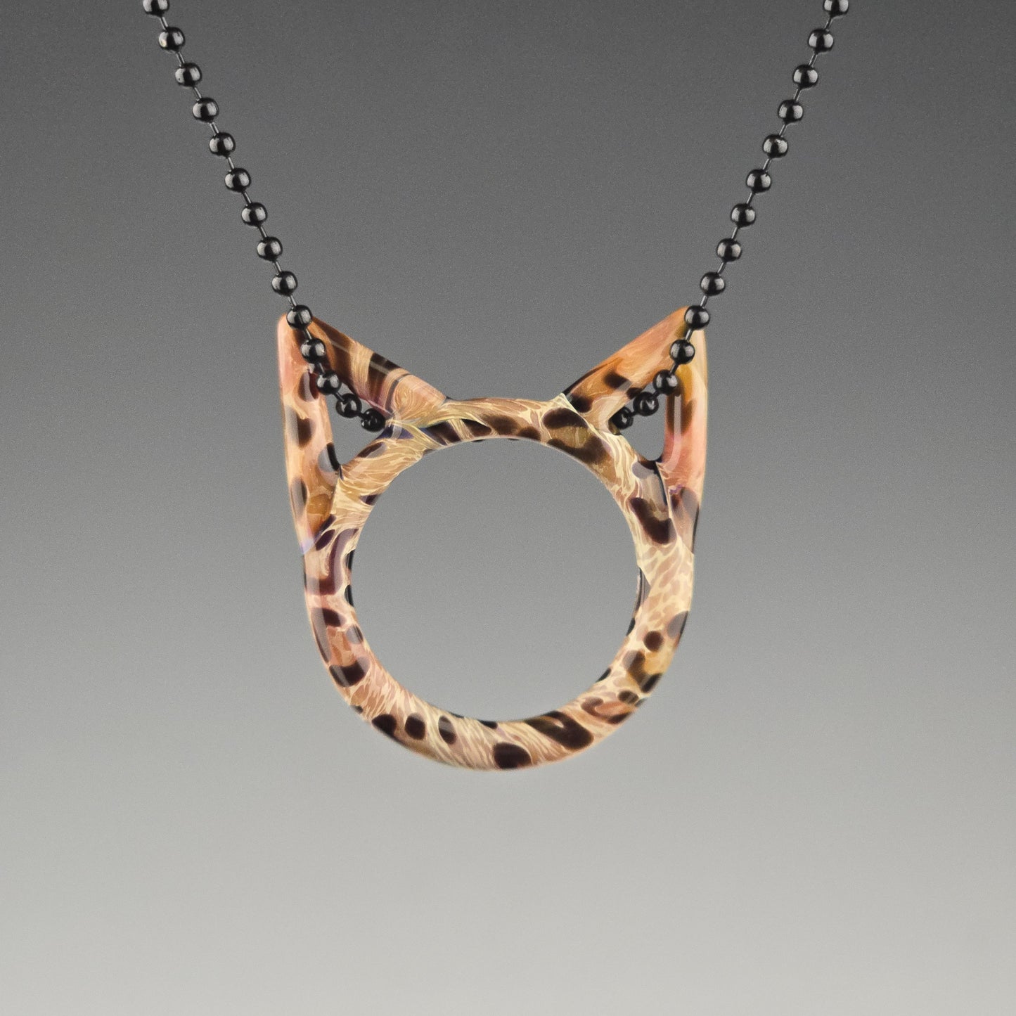 A handcrafted glass pendant in the shape of a kitty face with Bengal cat pattern hanging on a black chain