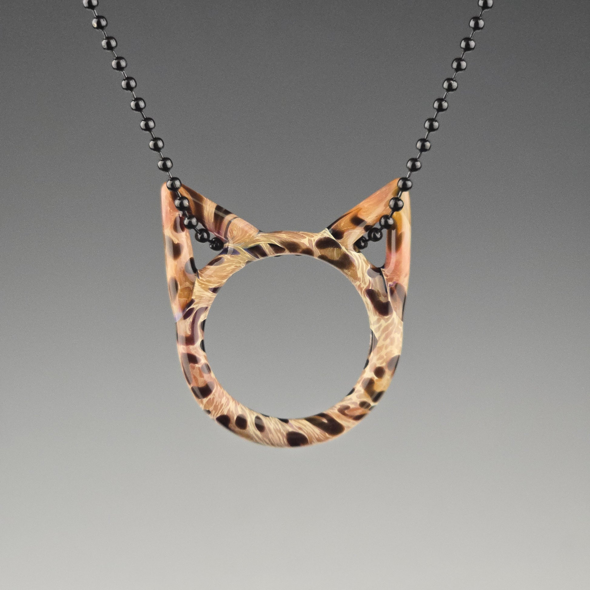 A handcrafted glass pendant in the shape of a kitty face with Bengal cat pattern hanging on a black chain
