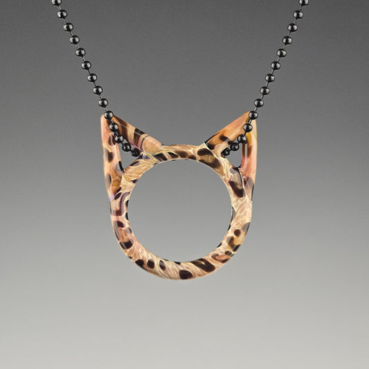 A handcrafted glass pendant in the shape of a kitty face with Bengal cat pattern hanging on a black chain