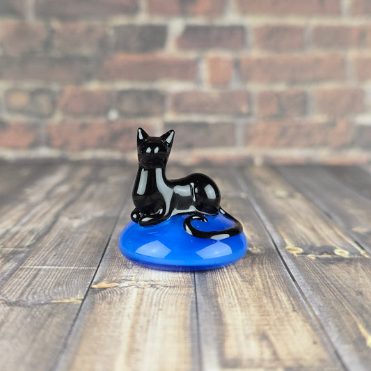 miniature sculpture of a black cat loafing on a sparkly blue pillow