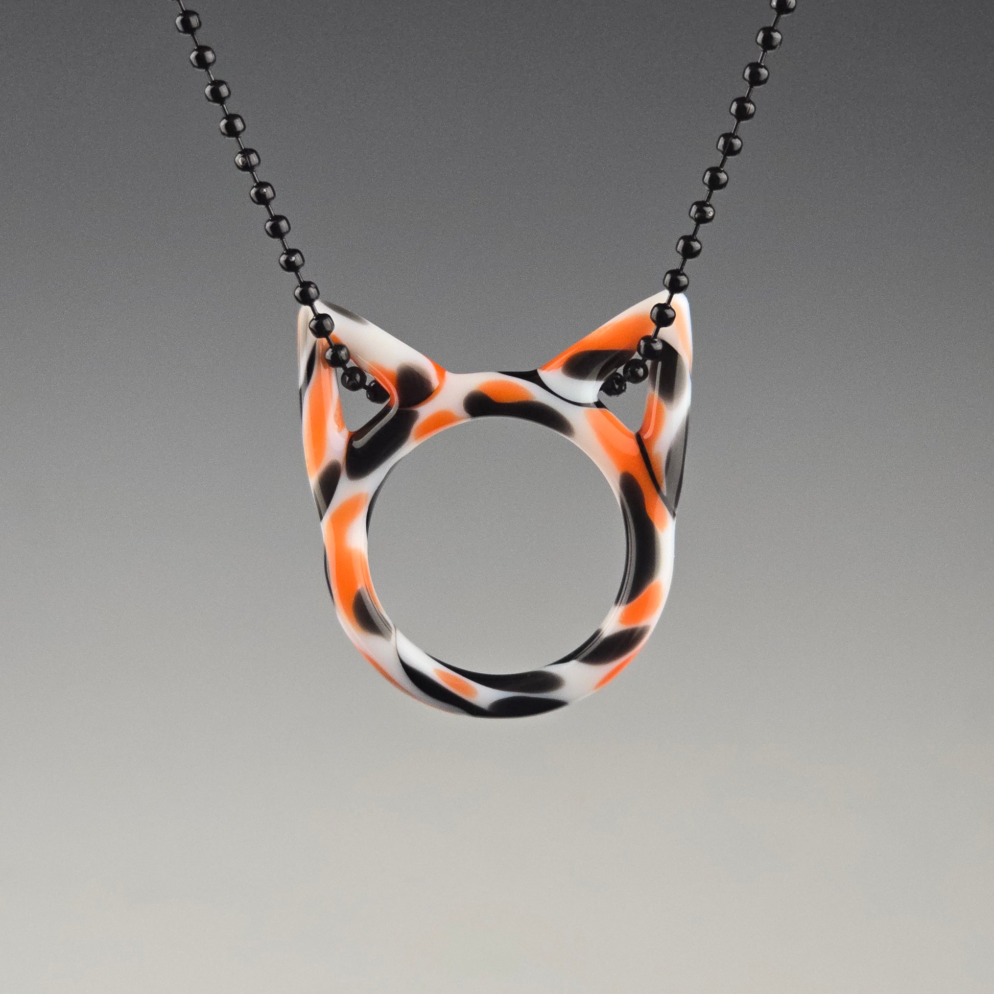 kitty face pendant featuring a calico pattern in black, orange, and white colors, attached to a ball chain.