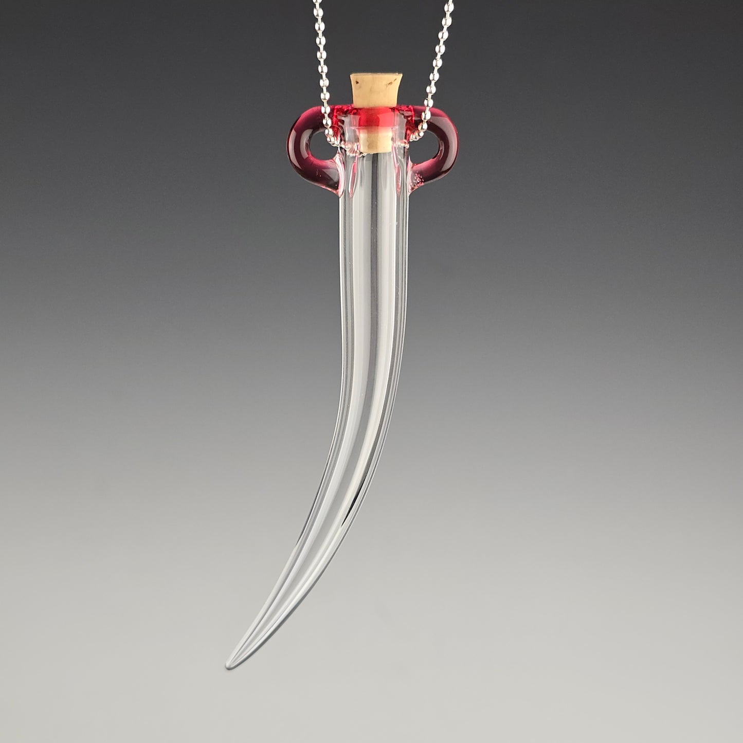 Keep the fallen whiskers you find safe inside this small hand blown hanging whisker shaped jar made out of clear glass with a pink tela magenta color accent around the corked opening.