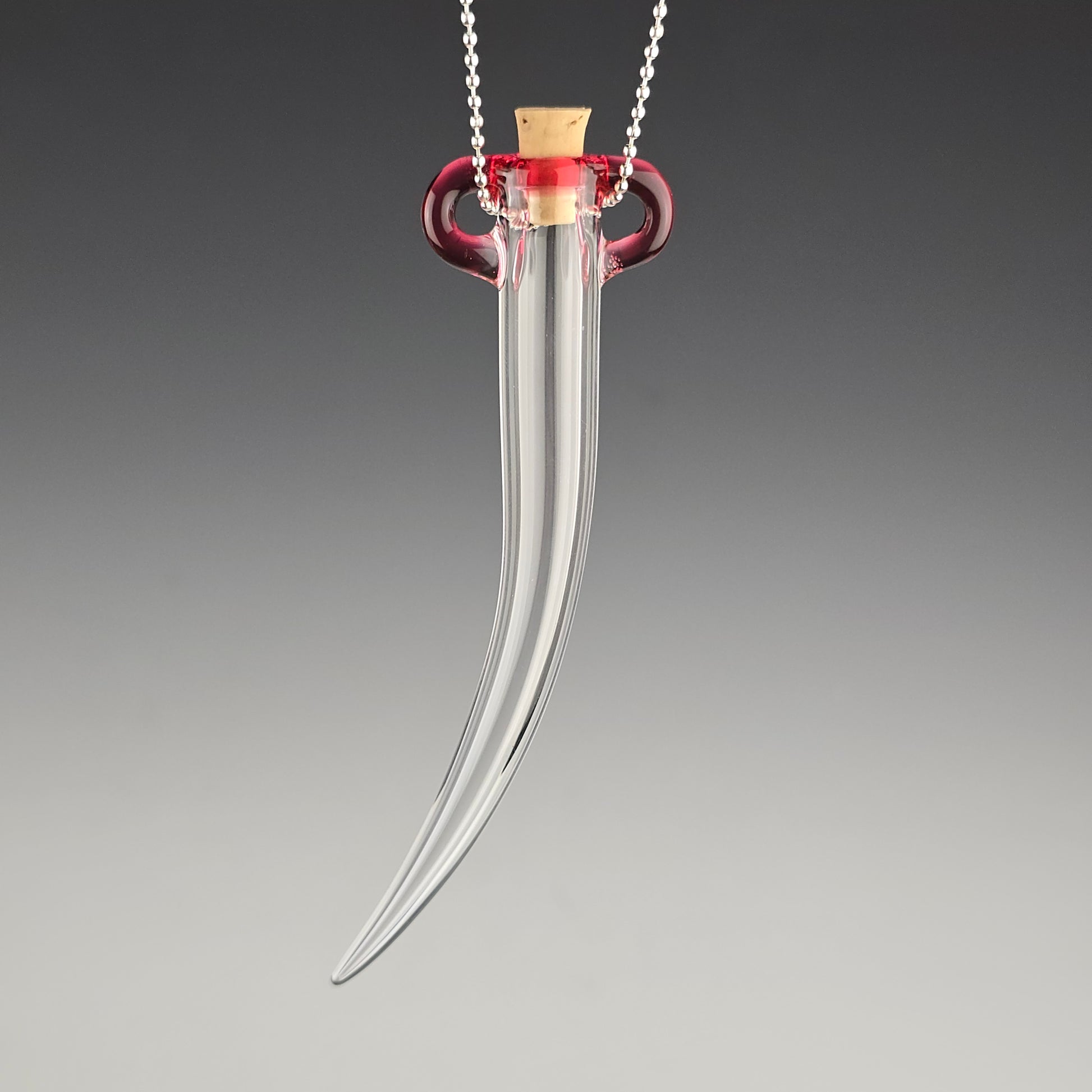 Keep the fallen whiskers you find safe inside this small hand blown hanging whisker shaped jar made out of clear glass with a pink tela magenta color accent around the corked opening.