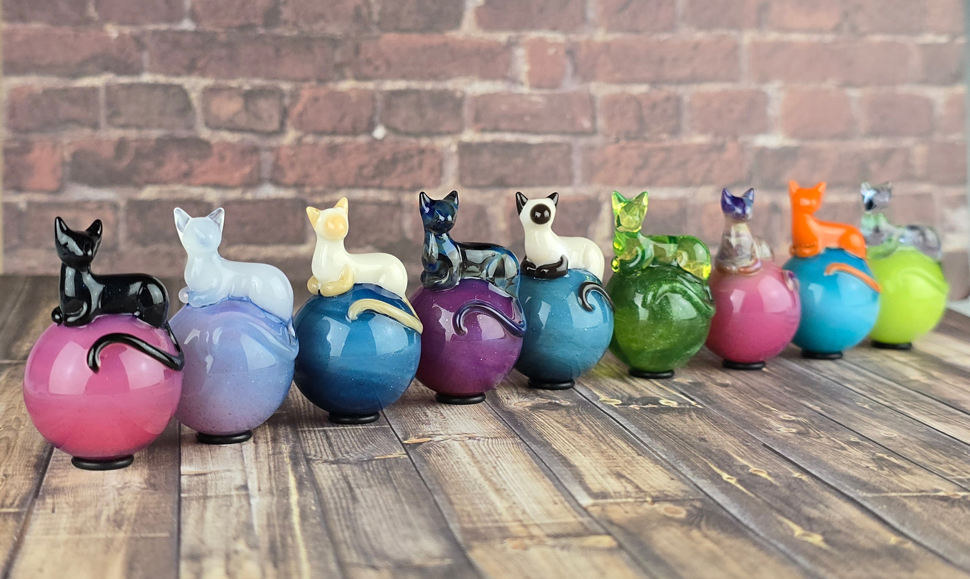 row of colorful glass marbles each with a small loafing cat sculpture on top