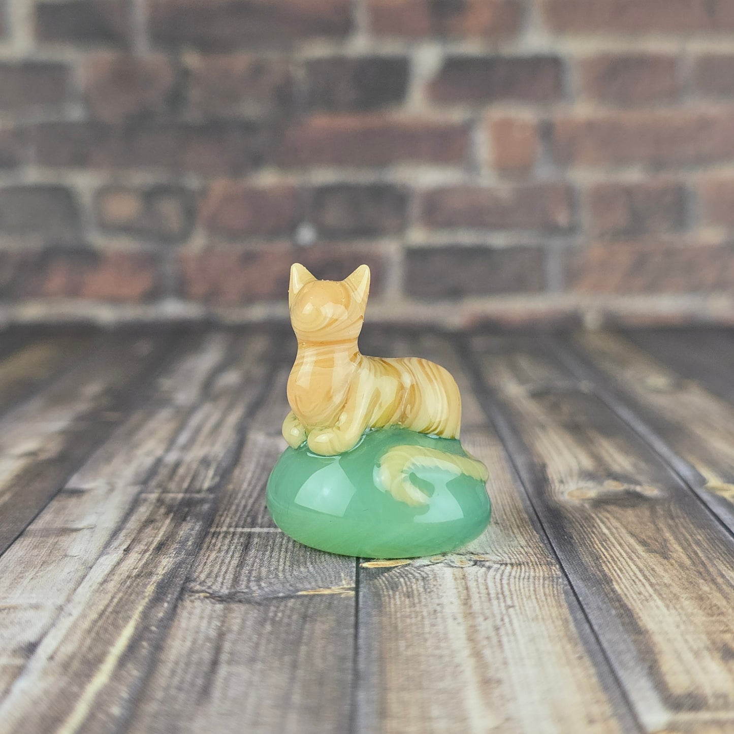 miniature sculpture of an orange tabby cat loafing on a jade green pillow