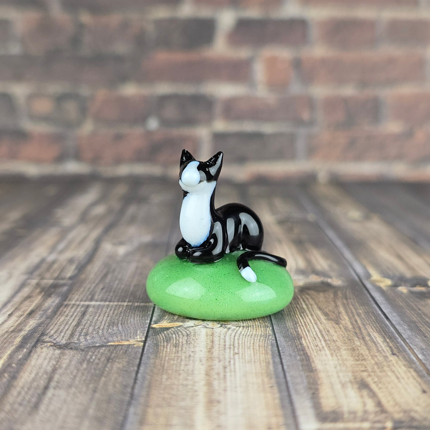 miniature sculpture of a tuxedo cat loafing on a sparkly jade green pillow